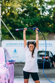 Woman with high pressure hose stands by car