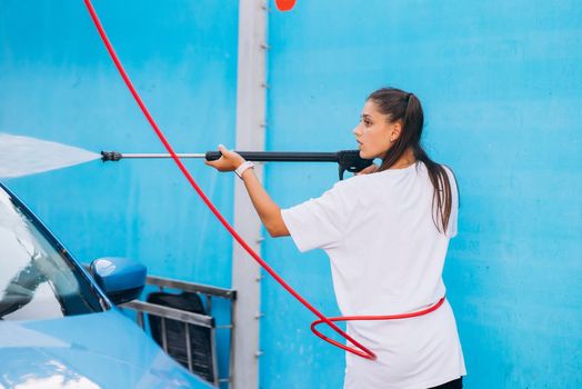 Brunette with two pigtails from a high-pressure hose washes the car at a car wash