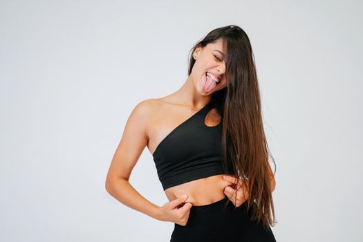 Young woman showing fat on her belly over white background. Lifestyle, sport, diet concept.