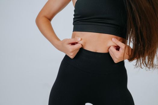 Young woman showing fat on her belly over white background. Lifestyle, sport, diet concept.