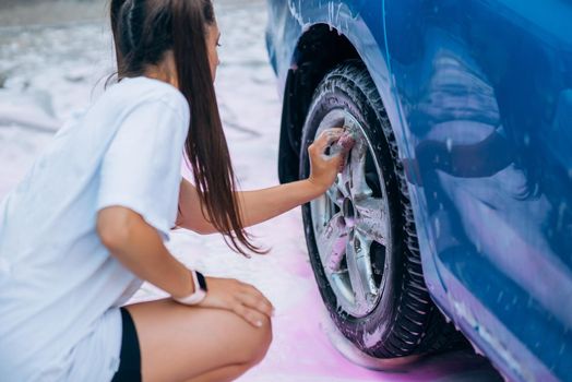 Brunette with two pigtails with a sponge washes the rim of a car