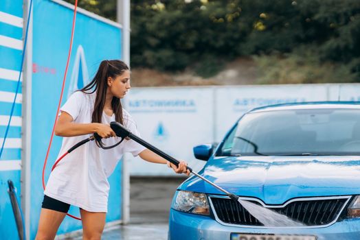 Brunette with two pigtails from a high-pressure hose washes the car at a car wash