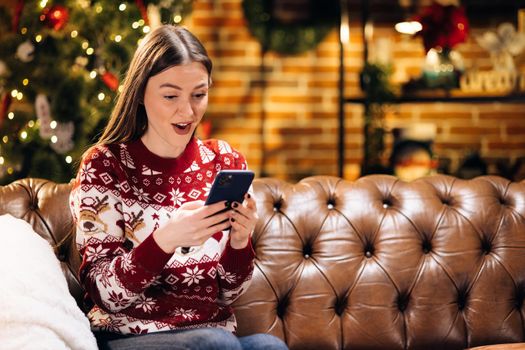 Happy laughing amazed caucasian woman looking at smartphone screen, getting message with unbelievable news, celebrating winning New Year or Christmas online lottery. Internet success concept.