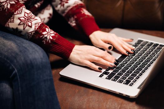 Hands working on laptop with christmas ornaments. Girl using laptop sitting on the sofa by christmas tree. Freelance and remote work during holidays. Christmas online store. Xmas shop. Christmas sales