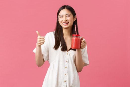 Healthy food, emotions and summer lifestyle concept. Upbeat happy, satisfied female cafe visitor enjoying delicious smoothie, showing thumbs-up as recommend drink, pink background.