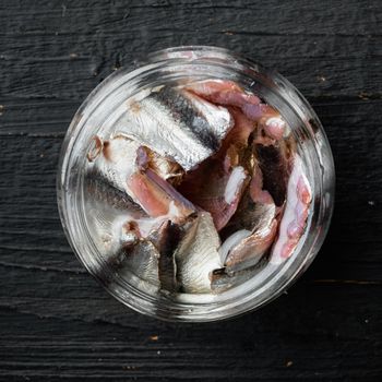 Pickled salted anchovies fillet set, in glass jar, on black wooden table background, top view flat lay, square format