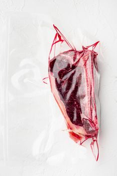 Dry aged beef marbled meat, raw fresh club beefsteak in plastic package set, on white stone surface, top view flat lay