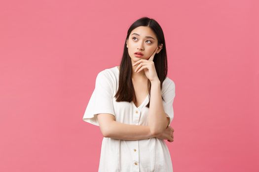 Beauty, people emotions and summer leisure concept. Annoyed and exhausted asian girl eye roll, looking away and exhale irritated, feeling bothered by someone, pink background.