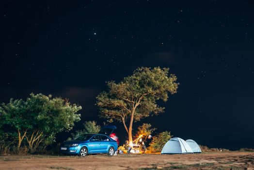 Group of five travellers rest on sea shore under tree on blue evening sky background. Tourism and camping concept.