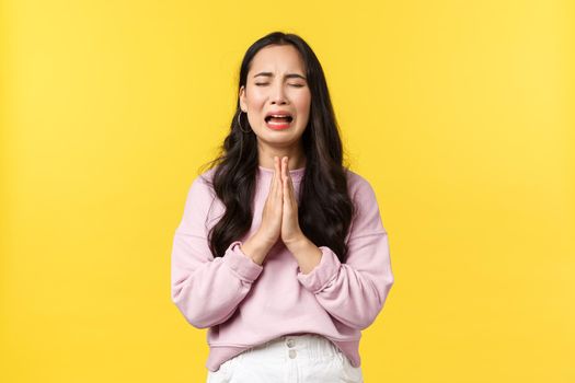 People emotions, lifestyle and fashion concept. Desperate and sad gloomy asian girl begging for forgiveness, crying heart out and praying, pleading god mercy, standing yellow background.
