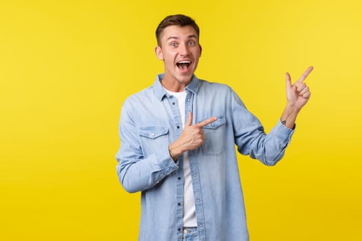 Good-looking happy man in casual clothes pointing fingers upper right corner and smiling excited, checking out awesome promo offer, demonstrate banner with advertisement, yellow background.