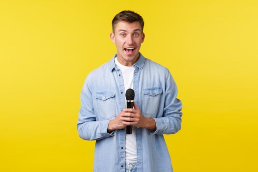 Lifestyle, people emotions and summer leisure concept. Lively happy handsome blond man looking away and smiling, talking on stage, perform stand-up or singing karaoke with microphone.
