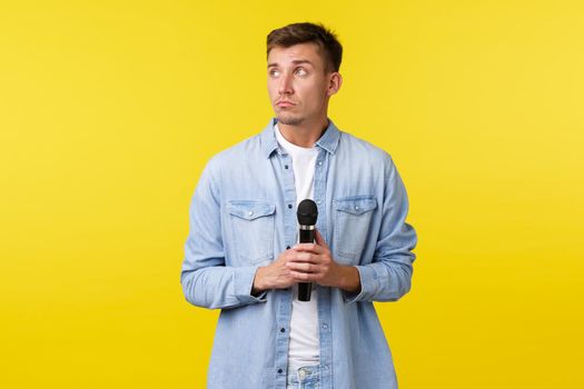 Lifestyle, people emotions and summer leisure concept. Thoughtful dreamy handsome man looking away, thinking as holding microphone, standing yellow background indecisive.