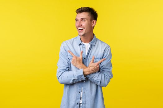 Portrait of handsome smiling blond man in casual clothes laughing and looking left while pointing sideways. Cheerful male customer shopping in store, make choice between two variants.