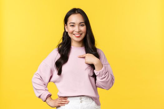 People emotions, lifestyle and fashion concept. Confident pretty and stylish asian woman in casual outfit pointing herself, propose own candidature, smiling pleased, stand yellow background.