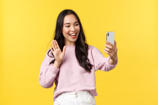 People emotions, lifestyle leisure and beauty concept. Cute outgoing asian girl talking on videocall with friends, waving hand to say hi at phone camera, blogger have live stream, yellow background.