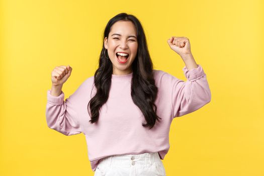 Lifestyle, emotions and advertisement concept. Happy smiling and pumped asian girl celebrating victory, chanting yes with hands raised up and broad grin, triumphing over achievement or success.