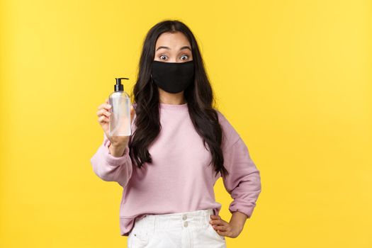 Covid-19, social-distancing lifestyle, prevent virus spread concept. Surprised asian girl in face mask always using hand sanitizer during coronavirus pandemic, recommend hygiene product.