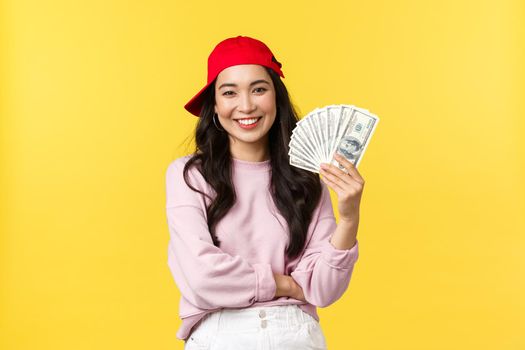 People emotions, lifestyle leisure and beauty concept. Young stylish female korean freelancer in red hipster cap, showing money she earned working from home, smiling carefree.