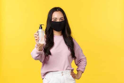 Covid-19, social-distancing lifestyle, prevent virus spread concept. Cheerful asian girl in face mask always using hand sanitizer during coronavirus pandemic, recommend hygiene product.