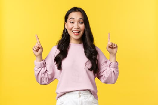 People emotions, lifestyle and fashion concept. Smiling female student showing summer vacation offers, special promo or discounts at store, pointing fingers up and smiling, yellow background.