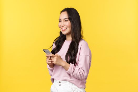 People emotions, lifestyle leisure and beauty concept. Profile shot of smiling japanese girl using smartphone and looking left pleased. Dreamy asian woman using carsharing app to call taxi.
