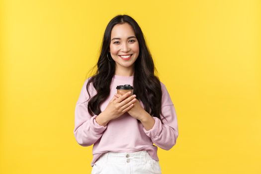 People emotions, lifestyle leisure and beauty concept. Lovely asian woman with cup of takeaway coffee enjoying summer weekends, smiling delighted and cute, drinking beverage over yellow background.
