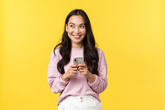 People emotions, lifestyle leisure and beauty concept. Dreamy and excited happy young asian woman using mobile phone, smiling and looking upper left corner thoughtful, have idea.