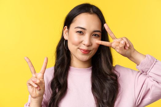 People emotions, lifestyle leisure and beauty concept. Kawaii pretty japanese girl showing peace signs and smiling cute, standing over yellow background advertising product.