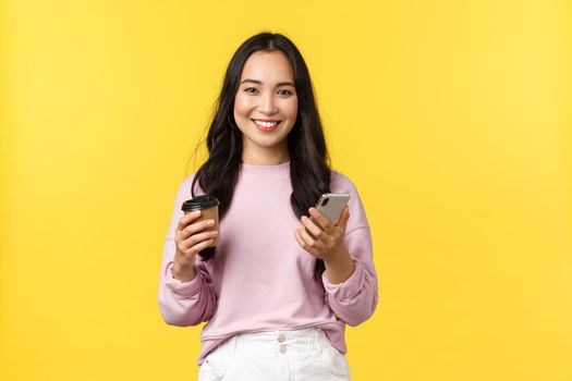 People emotions, lifestyle leisure and beauty concept. Attractive female student, college girl drinking takeaway coffee and checking messages on mobile phone, smiling at camera.