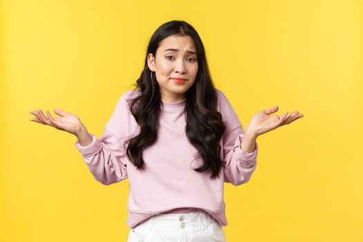 People emotions, lifestyle and fashion concept. Indecisive and clueless cute asian woman shrugging, smirk perplexed and shaking head, dont know, cant understand anything, yellow background.