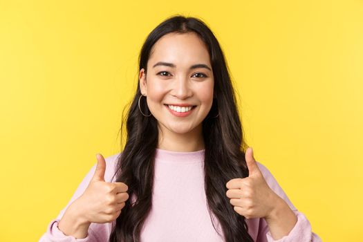 People emotions, lifestyle leisure and beauty concept. Upbeat smiling asian girl showing thumbs-up in approval, standing yellow background, agree and support idea, yellow background.