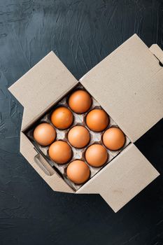 Fresh eggs on paper egg box set, on black background, top view flat lay