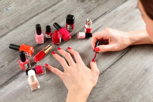 Top view on young woman hands, applying second layer of nail polish, with more bottles of lacquer in background. All trademarks blurred/cloned out.