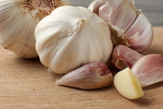 Garlic bulbs and cloves, one of them peeled and cut in half, on old scratched cutting board.