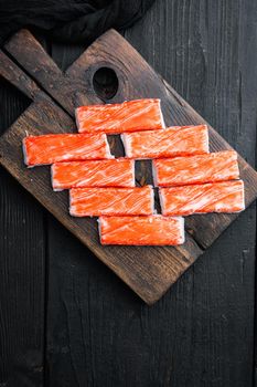 Fresh Crab meat stick surimi set, on wooden cutting board, on black wooden table background, top view flat lay