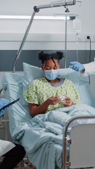 Team of doctors doing consultation with woman during pandemic in hospital ward. Specialists using digital tablet to cure ill patient with prescription medicine, wearing face masks.