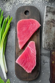 Fresh raw tuna fish steak with green pea, sesame and spring onions set, on wooden cutting board, and old butcher cleaver knife, on gray stone background, top view flat lay