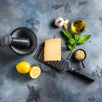 Green basil pesto italian recipe ingredients . Parmesan cheese, basil leaves, pine nuts, olive oil, garlic, salt, pepper and mortar. on gray concrete scratches stone background top view.