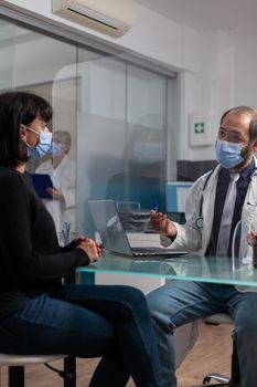 Doctor and patient discussing about health care at appointment in cabinet. Medic talking to woman about prescription medicine and treatment during coronavirus pandemic. Annual checkup visit