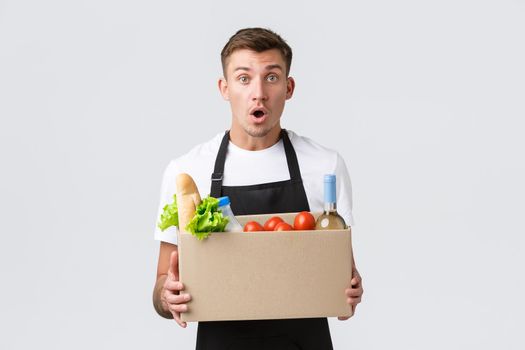 Retail, grocery shopping and delivery concept. Excited salesman announce awesome promo, holding box with groceries food, processing order, delivering food to customer, white background.