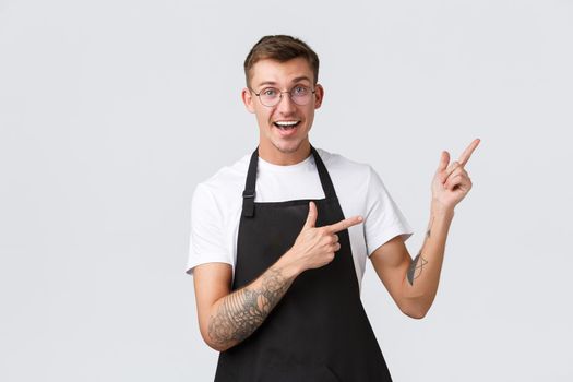 Small retail business owners, cafe and restaurant employees concept. Cheerful handsome barista, waiter inviting visit store, pointing upper right corner showing special discounts, white background.