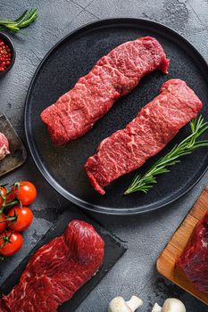 Raw set of denver steaks ob black plate raw organic food , marbled beef over other alternative cuts with herbs tomatoes peppercorns over grey stone surface background top view vertical