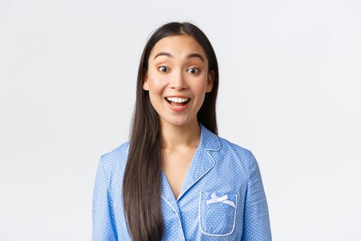 Close-up of enthusiastic and upbeat asian girl in blue pajama looking with thrill at camera. Female student in jammies hear great announcement, being interested in promo, white background.