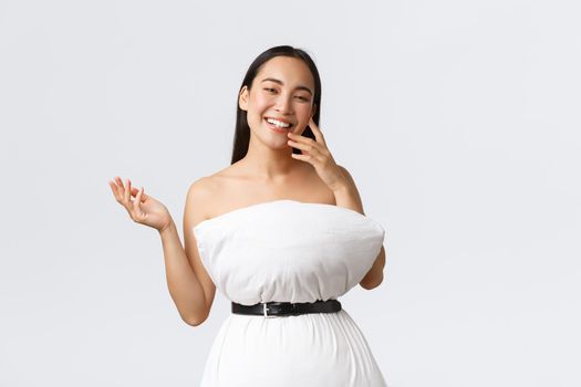 Beauty, fashion and social media concept. Pretty happy asian woman laughing and show-off her new outfit made of pillow and belt, posing in pillow dress over white background.