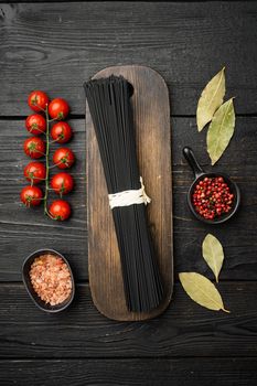 Squid ink black tinted twirl of raw tagliatelle set, on black wooden table background, top view flat lay