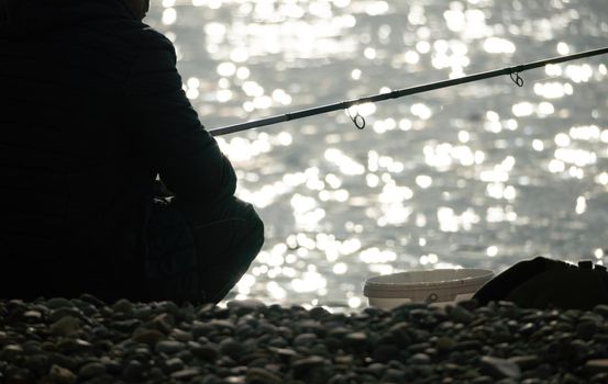 Man hobby fishing on sea tightens a fishing line reel of fish summer. Calm surface sea. Close-up of a fisherman hands twist reel with fishing line on a rod. Fishing in the blue sea outdoors