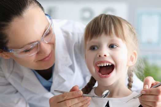 Portrait of child visiting family doctor, pediatrician with tool check throat, girl open mouth wide. Healthcare, child care, medicine, childhood concept