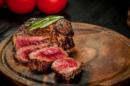 Grill juicy beef steak with salt pepper and rosemary on a wooden board with a knife and fork. Still life