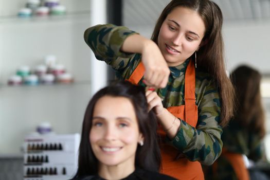 Portrait of smiling hairdresser creating fancy hairstyle for female client. Prepare woman for important event in beauty salon. Wellness, barbershop concept